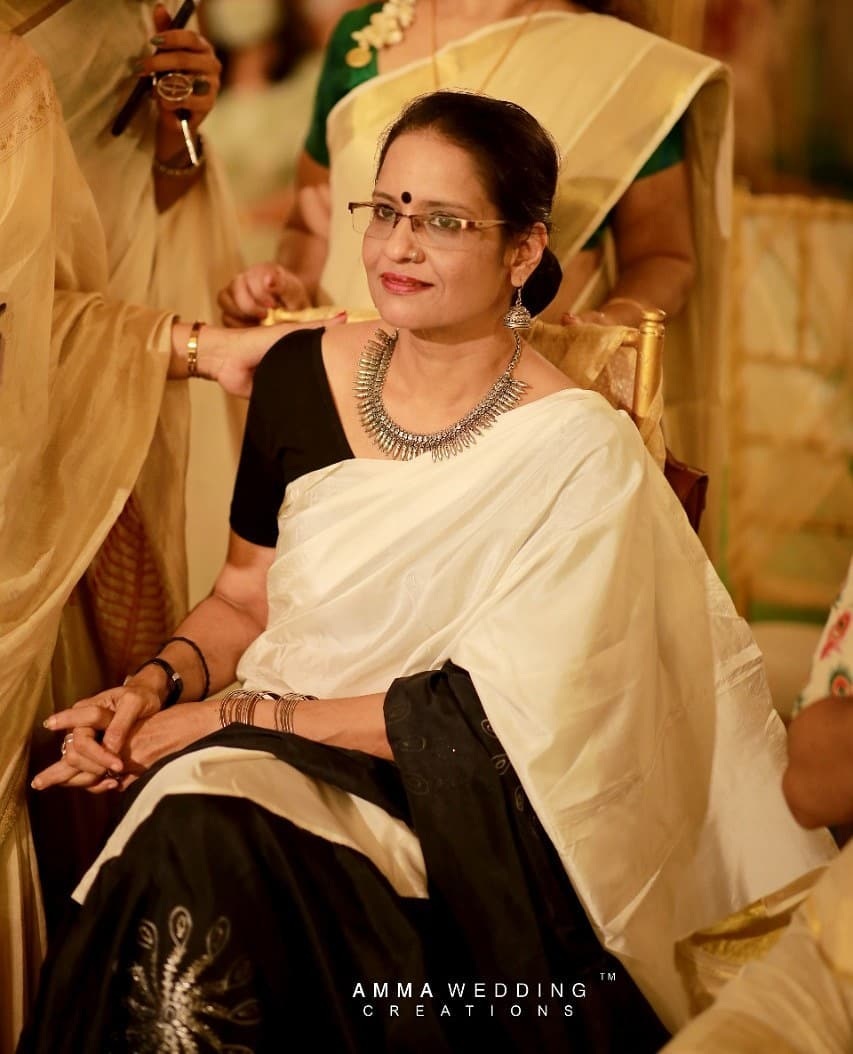 A woman in a white and black saree, sitting gracefully.